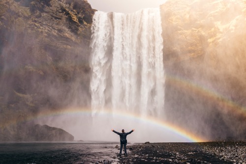 Man standing at rainbow and waterfall